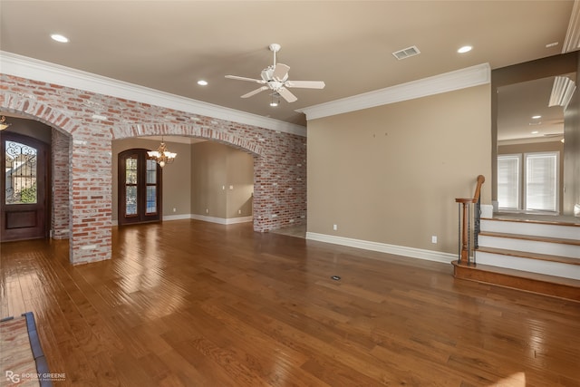 unfurnished living room with ornamental molding, dark hardwood / wood-style floors, brick wall, and ceiling fan with notable chandelier