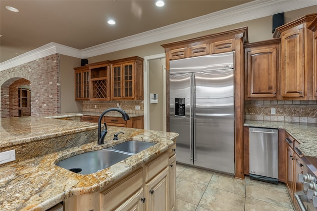 kitchen featuring light stone countertops, sink, backsplash, built in refrigerator, and ornamental molding