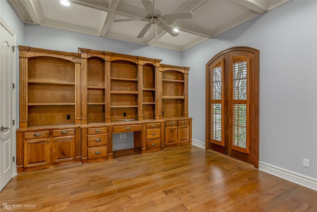 unfurnished office with coffered ceiling, built in desk, beamed ceiling, ceiling fan, and light hardwood / wood-style floors