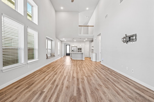 unfurnished living room featuring light wood-type flooring, a towering ceiling, and ceiling fan