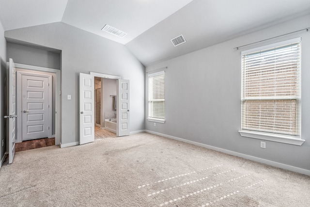 unfurnished bedroom featuring light carpet, ensuite bath, and lofted ceiling