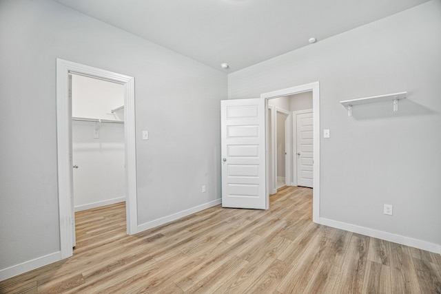 unfurnished bedroom featuring a closet, a walk in closet, and light hardwood / wood-style flooring