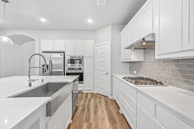 kitchen with light wood-type flooring, stainless steel appliances, decorative light fixtures, white cabinets, and range hood