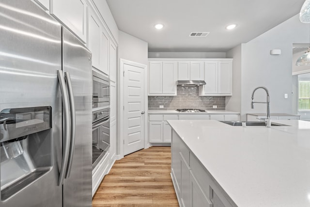 kitchen featuring white cabinetry, sink, light hardwood / wood-style flooring, decorative backsplash, and appliances with stainless steel finishes