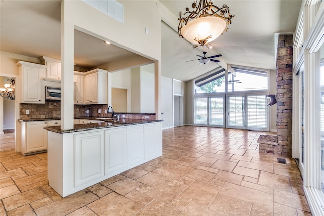 kitchen with decorative backsplash, kitchen peninsula, dark stone counters, sink, and ceiling fan