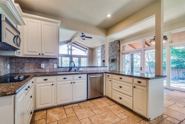 kitchen featuring kitchen peninsula, ceiling fan, dark stone counters, sink, and stainless steel appliances