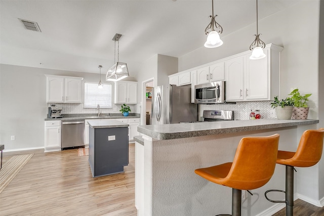 kitchen featuring pendant lighting, stainless steel appliances, kitchen peninsula, and white cabinets