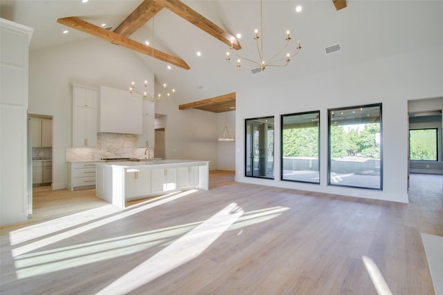 kitchen featuring white cabinetry, hanging light fixtures, beamed ceiling, decorative backsplash, and a center island with sink