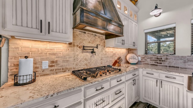 kitchen featuring light stone countertops, custom exhaust hood, white cabinetry, decorative backsplash, and stainless steel gas cooktop