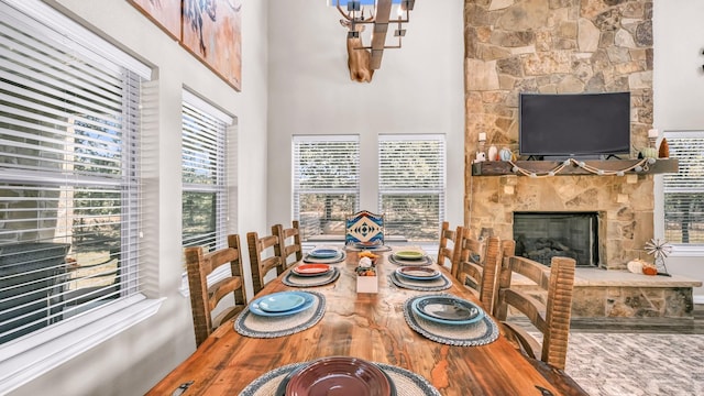 dining area featuring a wealth of natural light, a stone fireplace, and an inviting chandelier