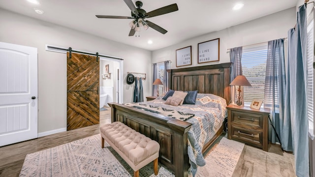 bedroom featuring light wood-type flooring, ceiling fan, and a barn door