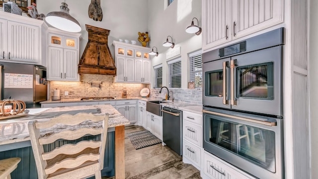 kitchen featuring appliances with stainless steel finishes, white cabinetry, sink, a breakfast bar, and custom range hood