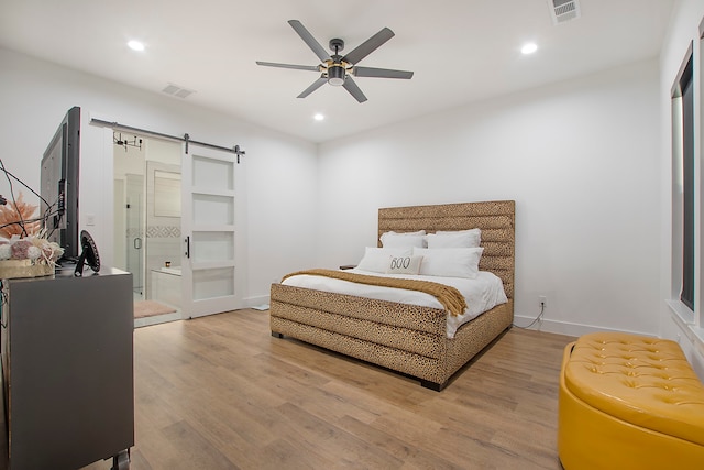 bedroom featuring a barn door, light wood-type flooring, and ceiling fan