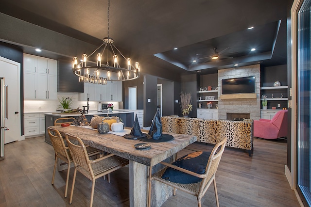 dining space featuring a fireplace, hardwood / wood-style flooring, a notable chandelier, a raised ceiling, and built in shelves