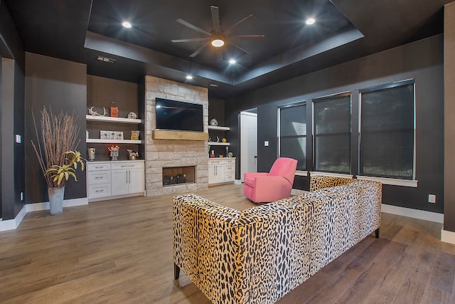 living room with hardwood / wood-style flooring, a raised ceiling, and a fireplace