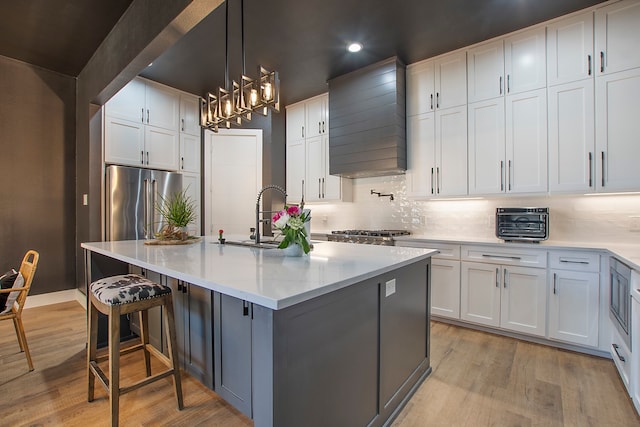 kitchen with premium range hood, white cabinets, a kitchen island with sink, and light wood-type flooring