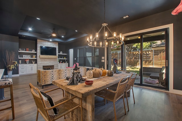 dining room with a stone fireplace, a tray ceiling, built in features, and dark hardwood / wood-style flooring