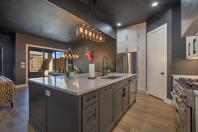 kitchen featuring an island with sink, high end appliances, sink, pendant lighting, and white cabinetry