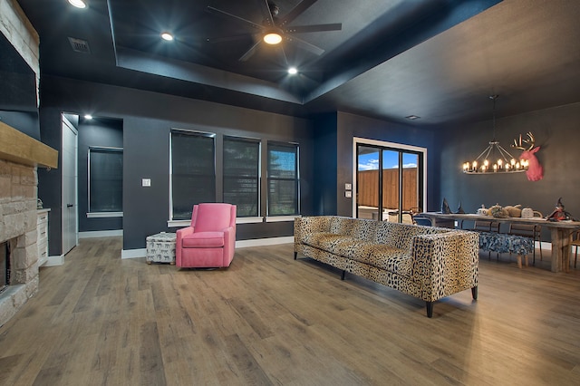 living room featuring hardwood / wood-style floors, a fireplace, a tray ceiling, and ceiling fan