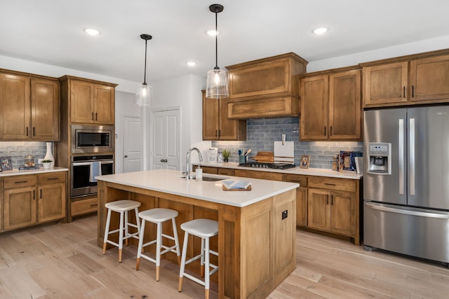 kitchen featuring appliances with stainless steel finishes, light hardwood / wood-style flooring, sink, and an island with sink