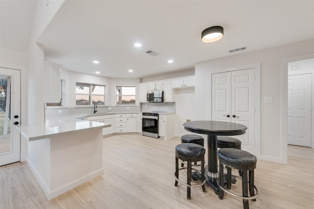 kitchen with kitchen peninsula, white cabinetry, sink, light hardwood / wood-style floors, and stainless steel appliances