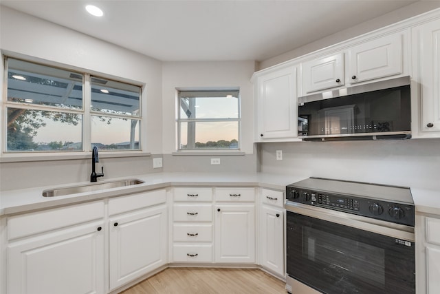 kitchen with stainless steel appliances, sink, light wood-type flooring, and white cabinets