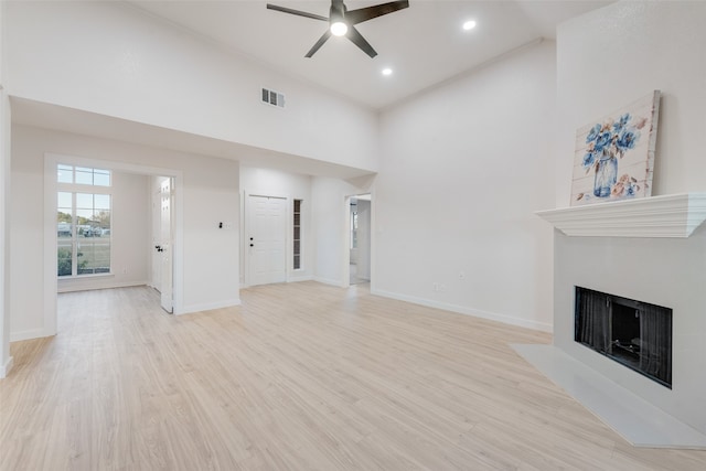 unfurnished living room with a towering ceiling, light wood-type flooring, and ceiling fan