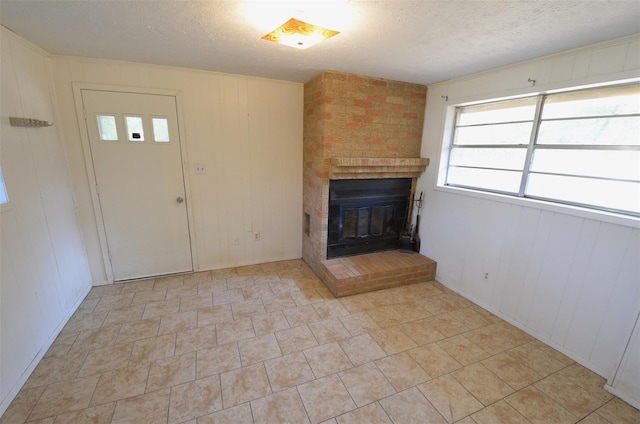 unfurnished living room featuring wooden walls, a brick fireplace, and a textured ceiling