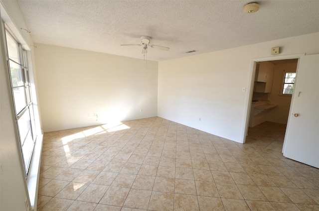 unfurnished room with a textured ceiling, light tile patterned flooring, and ceiling fan