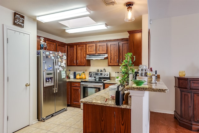 kitchen featuring stainless steel appliances, light tile patterned flooring, kitchen peninsula, light stone countertops, and a skylight