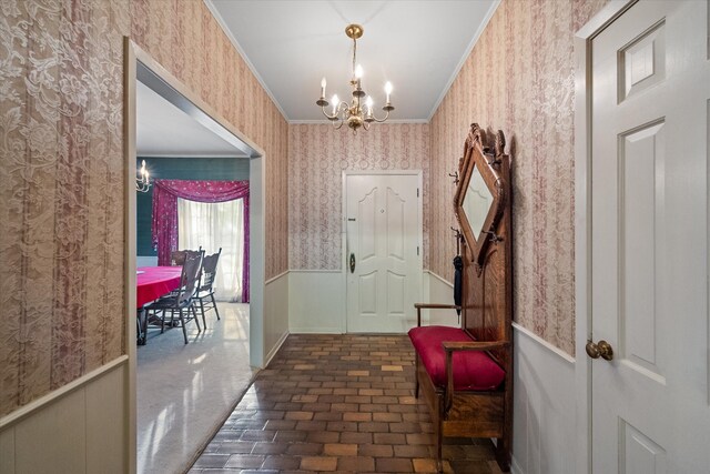 entryway with crown molding, a notable chandelier, and dark colored carpet