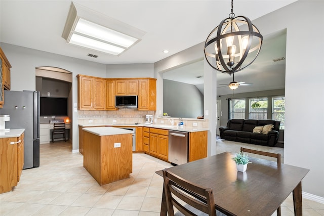 kitchen with ceiling fan with notable chandelier, a kitchen island, stainless steel appliances, decorative backsplash, and light tile patterned floors