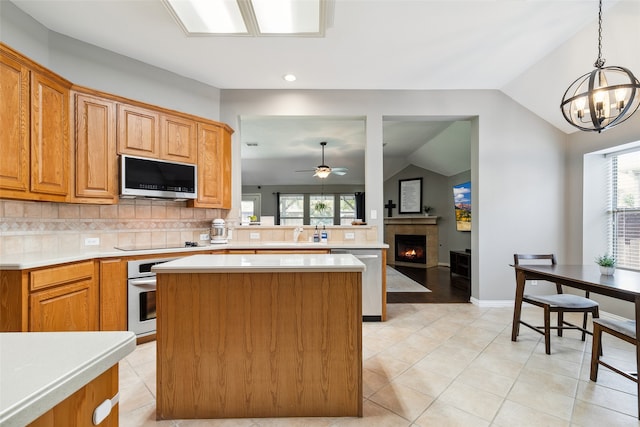 kitchen with appliances with stainless steel finishes, a tile fireplace, hanging light fixtures, vaulted ceiling, and decorative backsplash