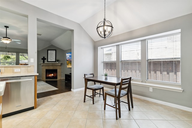 dining room with ceiling fan with notable chandelier, light tile patterned floors, lofted ceiling, and a fireplace