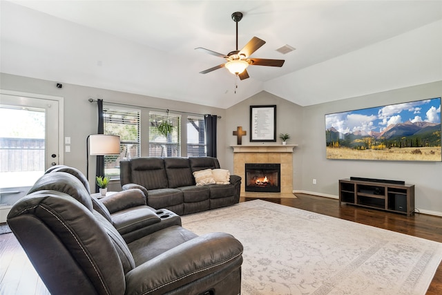 living room featuring vaulted ceiling, dark hardwood / wood-style floors, a tile fireplace, and ceiling fan