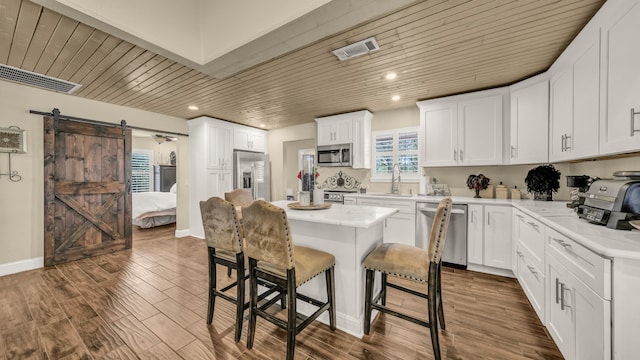 kitchen with appliances with stainless steel finishes, a barn door, a center island, dark hardwood / wood-style flooring, and white cabinetry