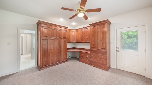 unfurnished office featuring built in desk, light carpet, and ceiling fan