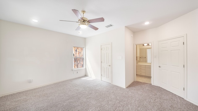 unfurnished bedroom featuring ensuite bathroom, light colored carpet, and ceiling fan