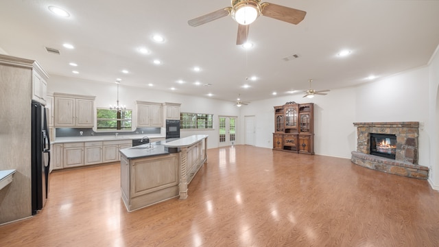 kitchen with cream cabinets, light wood-type flooring, a fireplace, a kitchen island, and stainless steel fridge