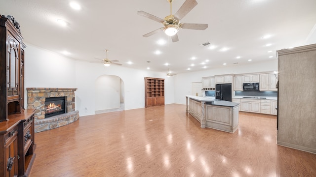 kitchen with black appliances, a fireplace, ceiling fan, light hardwood / wood-style flooring, and a center island with sink