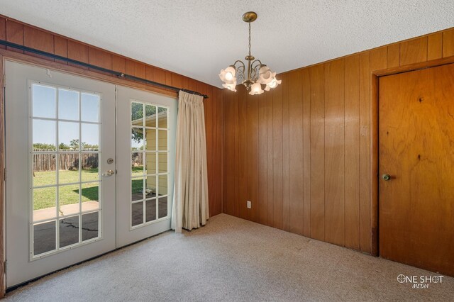 empty room featuring wood walls, french doors, a textured ceiling, and an inviting chandelier