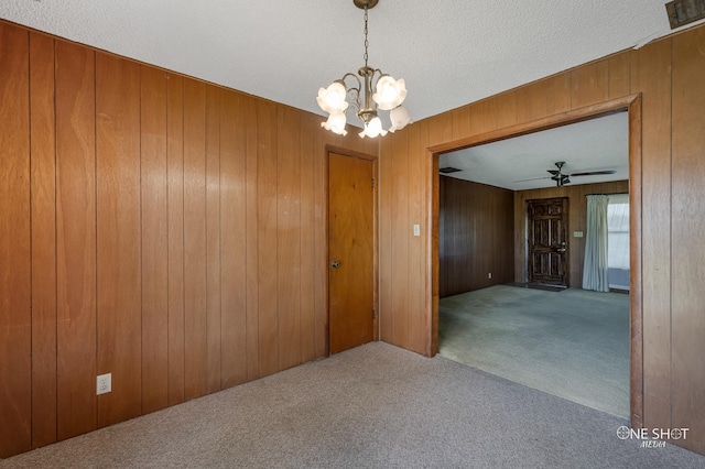 carpeted spare room with a textured ceiling, ceiling fan with notable chandelier, and wooden walls