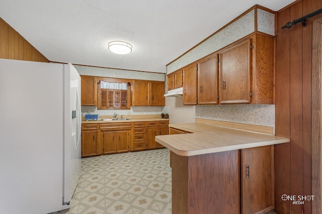 kitchen with white refrigerator with ice dispenser, a textured ceiling, kitchen peninsula, and sink