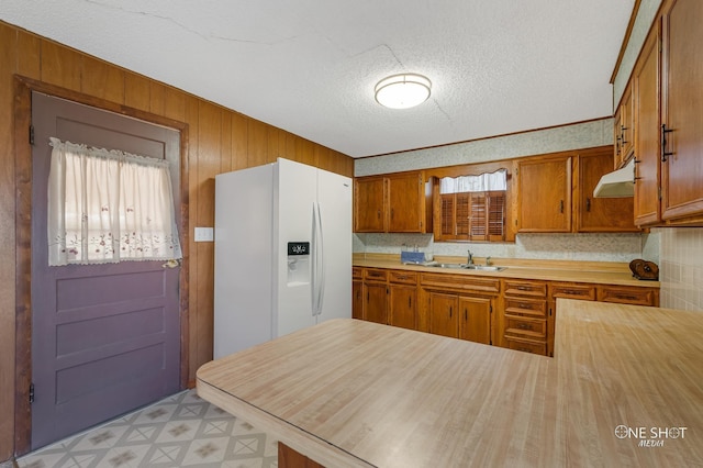 kitchen featuring kitchen peninsula, a textured ceiling, white fridge with ice dispenser, and sink