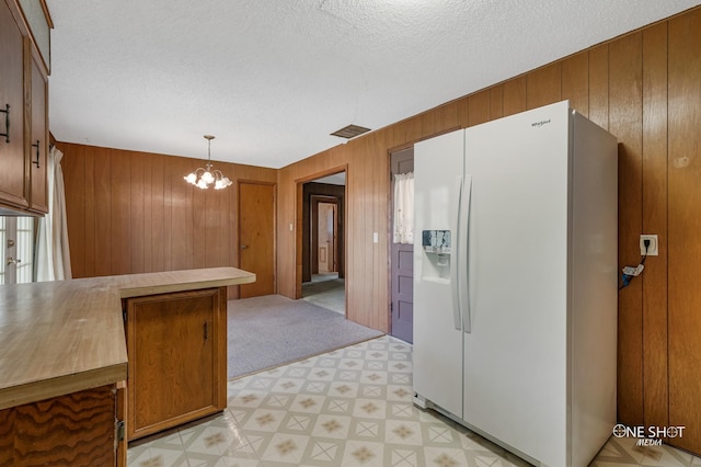 kitchen featuring white refrigerator with ice dispenser, decorative light fixtures, an inviting chandelier, and wooden walls