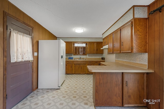 kitchen featuring a textured ceiling, kitchen peninsula, sink, and white refrigerator with ice dispenser