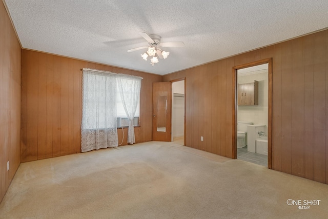 unfurnished bedroom with ceiling fan, wooden walls, and ensuite bath