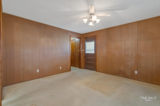 carpeted spare room with wooden walls, ceiling fan, and a textured ceiling