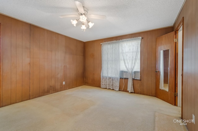 empty room featuring light carpet, a textured ceiling, ceiling fan, cooling unit, and wood walls