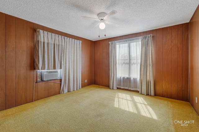 empty room featuring carpet, wood walls, cooling unit, ceiling fan, and a textured ceiling